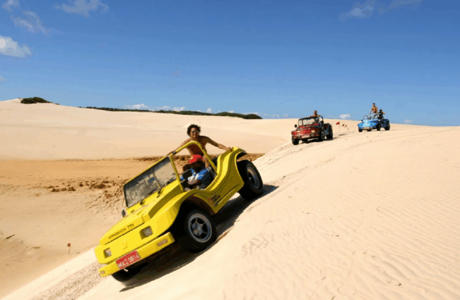 Pessoas passeando de buggy sobre as areias finas e claras da praia, ao fundo e céu aberto