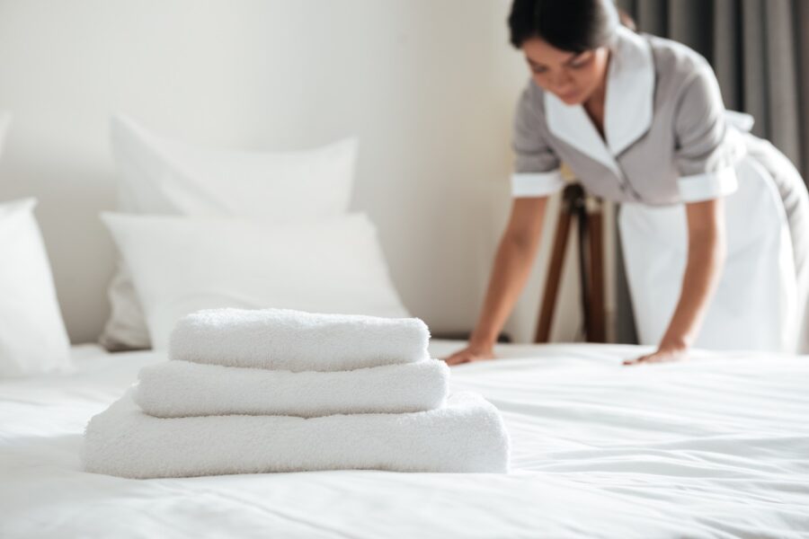 Roupa de cama na hospedagem: como elevar o padrão de qualidade do quarto 2 Camareira colocando roupa de cama de hotel