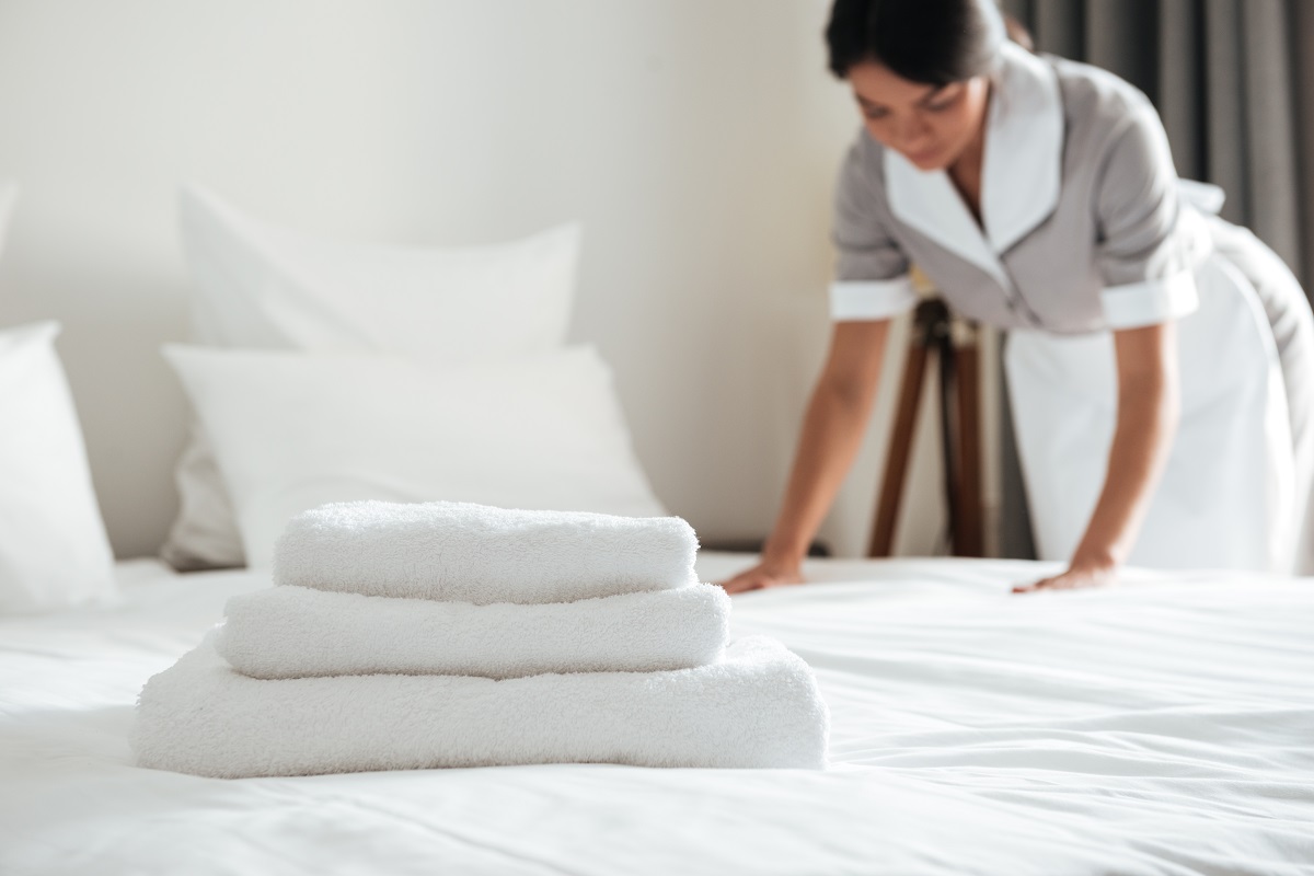 Roupa de cama na hospedagem: como elevar o padrão de qualidade do quarto 1 Camareira colocando roupa de cama de hotel